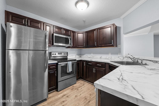 kitchen with dark brown cabinets, light stone counters, light wood-style floors, stainless steel appliances, and a sink