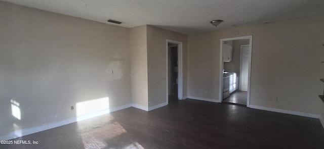 empty room featuring baseboards, visible vents, and dark wood-style floors