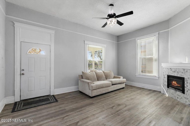 interior space featuring wood finished floors, baseboards, ceiling fan, a textured ceiling, and a glass covered fireplace