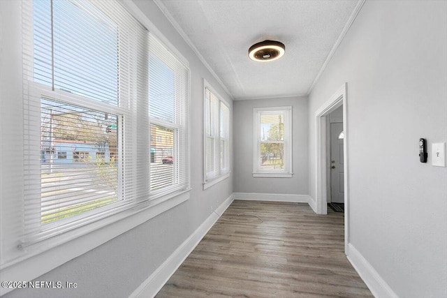 corridor featuring baseboards, a textured ceiling, wood finished floors, and crown molding