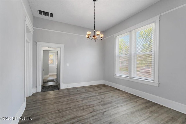 spare room featuring a wealth of natural light, visible vents, a notable chandelier, and wood finished floors