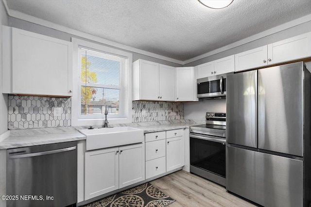 kitchen featuring backsplash, light wood-type flooring, white cabinets, stainless steel appliances, and a sink