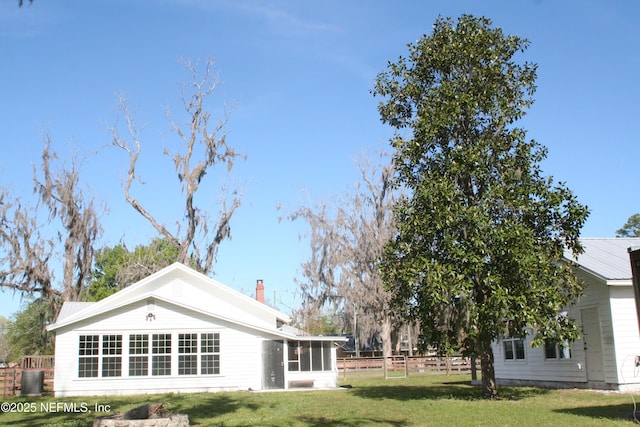 rear view of house with a chimney, a sunroom, fence, and a yard