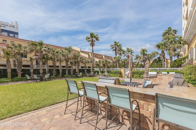 view of patio featuring fence, exterior kitchen, area for grilling, and outdoor wet bar