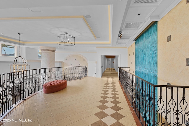 corridor with visible vents, a raised ceiling, an inviting chandelier, and an upstairs landing