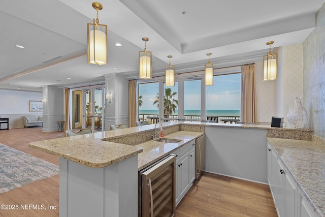 kitchen with beverage cooler, light stone countertops, hanging light fixtures, a wainscoted wall, and a sink