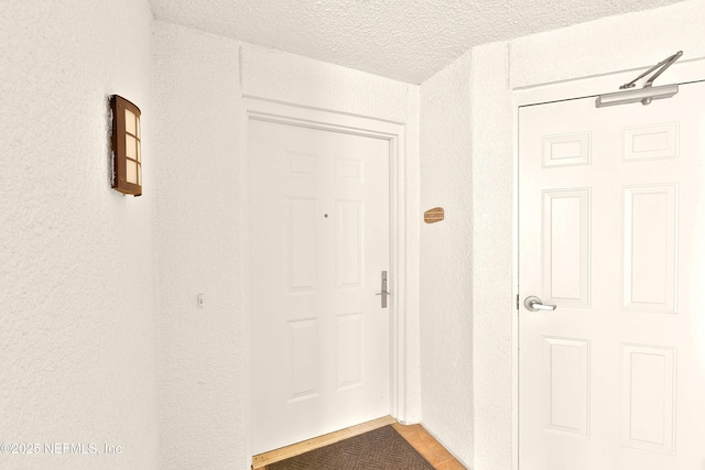 doorway to outside with a textured ceiling and a textured wall