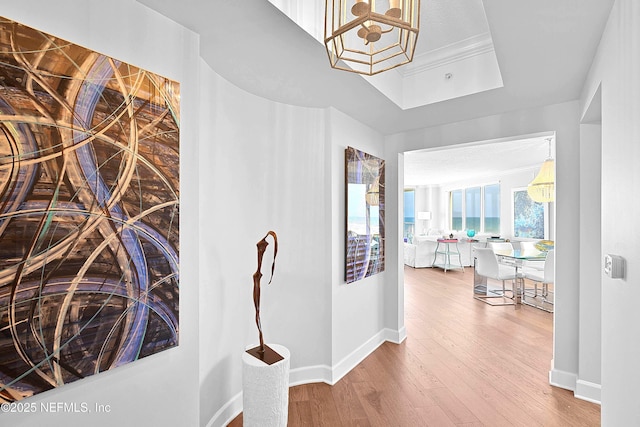 hall featuring a tray ceiling, a notable chandelier, wood finished floors, and baseboards
