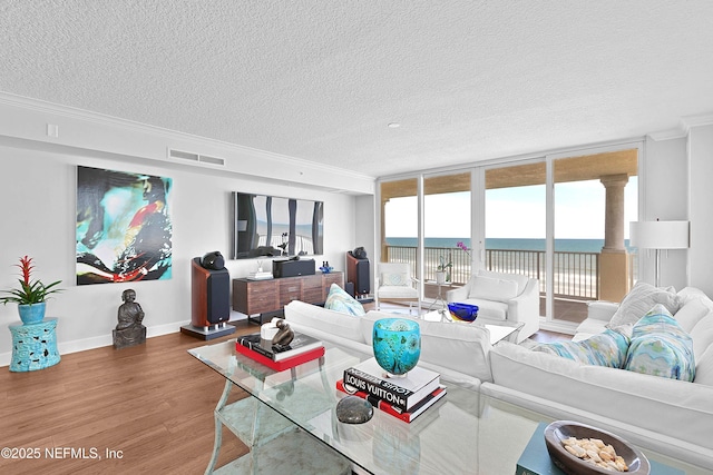 living area with a textured ceiling, crown molding, visible vents, baseboards, and wood finished floors