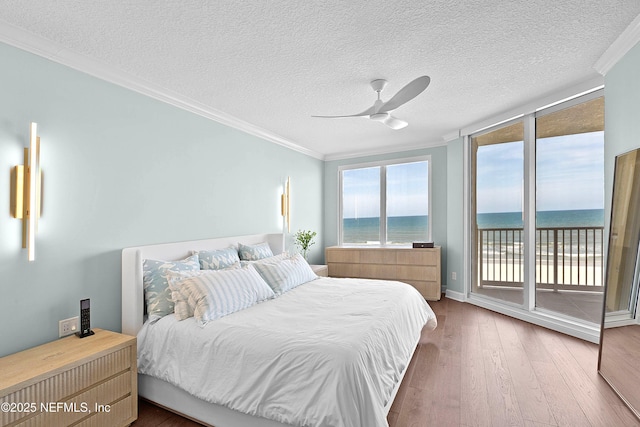 bedroom with a water view, wood finished floors, crown molding, and access to outside