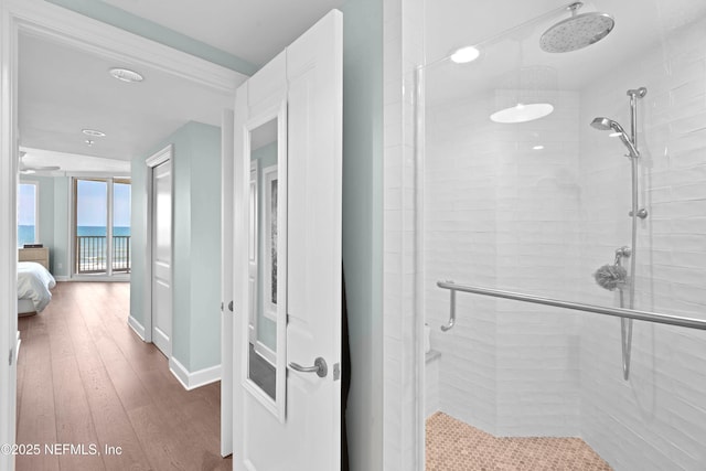 ensuite bathroom featuring ensuite bath, hardwood / wood-style floors, a shower stall, a water view, and baseboards