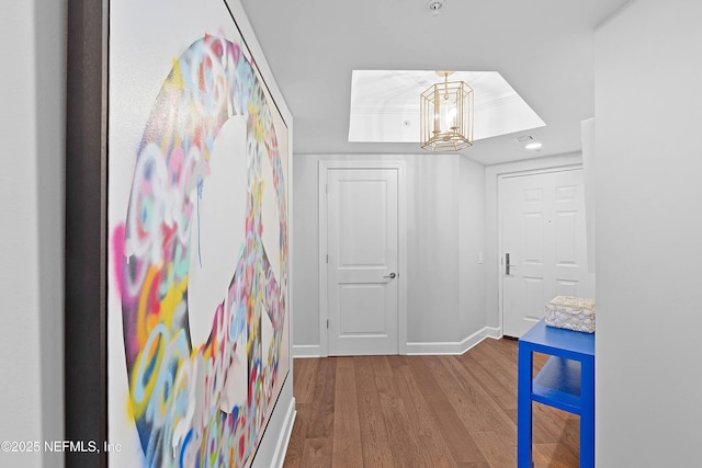 hallway featuring recessed lighting, an inviting chandelier, a tray ceiling, baseboards, and wood finished floors