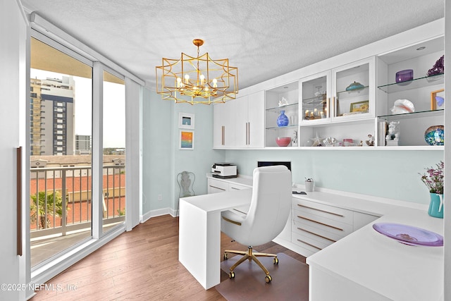 office area with a textured ceiling, an inviting chandelier, a wealth of natural light, and light wood-type flooring