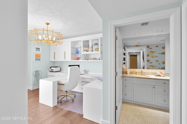 office with an inviting chandelier, a sink, light wood-style flooring, and visible vents