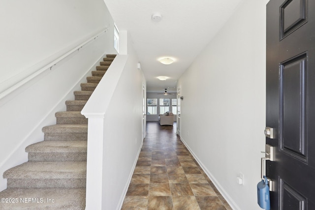 corridor with stairway, baseboards, and stone finish floor
