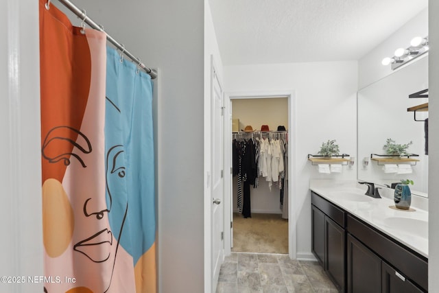 full bath with a textured ceiling, double vanity, a spacious closet, and a sink