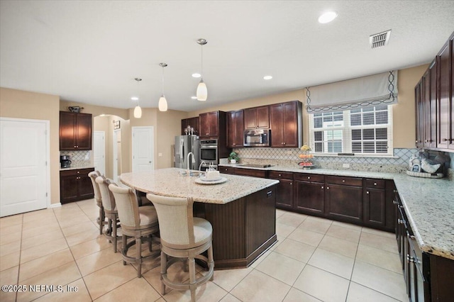 1074 Spanish Bay Ct, Orange Park, FL 32065 - kitchen with light tile patterned floors, stainless steel appliances, arched walkways, an island with sink, and light stone countertops