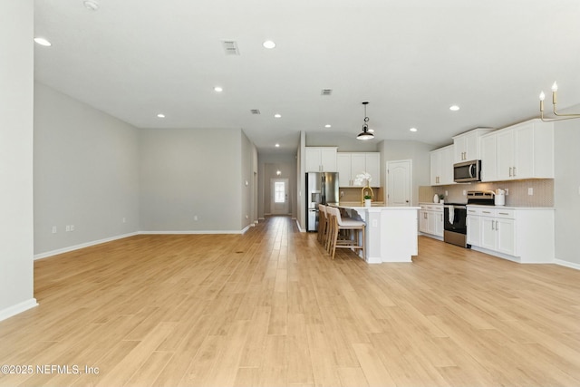 kitchen with light wood-type flooring, a kitchen breakfast bar, appliances with stainless steel finishes, and open floor plan
