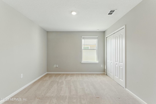 unfurnished bedroom featuring visible vents, a textured ceiling, a closet, carpet, and baseboards