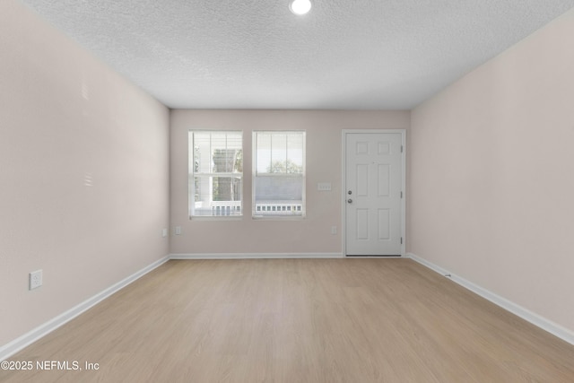 spare room with baseboards, light wood finished floors, and a textured ceiling