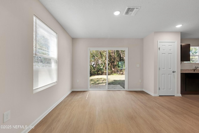 empty room with light wood-style floors, visible vents, and baseboards