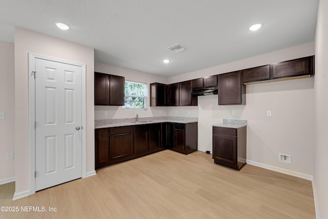 kitchen featuring visible vents, dark brown cabinets, light wood-style floors, and a sink