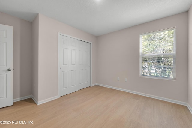 unfurnished bedroom with light wood-style floors, baseboards, and a closet