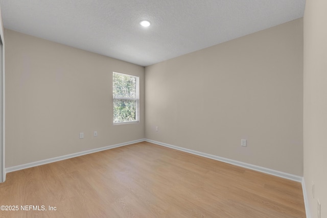empty room with baseboards, light wood finished floors, and a textured ceiling