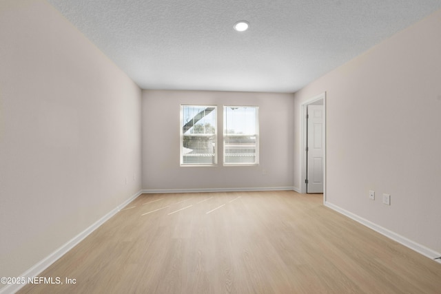 spare room with baseboards, a textured ceiling, and light wood finished floors