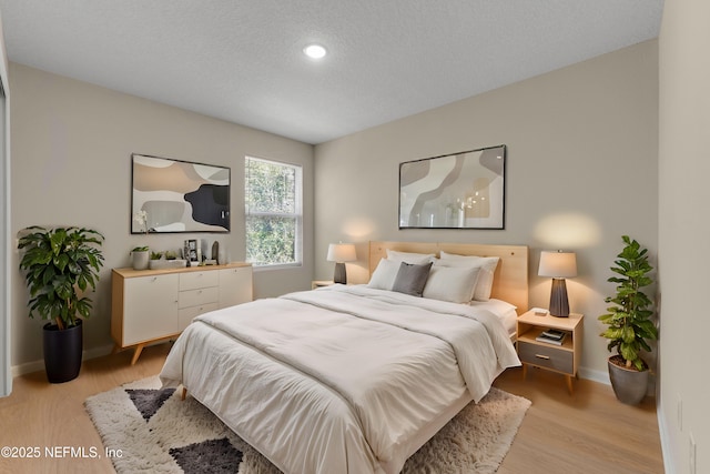 bedroom featuring light wood-style floors, baseboards, and a textured ceiling