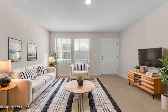 living area featuring baseboards, light wood-style floors, and a textured ceiling