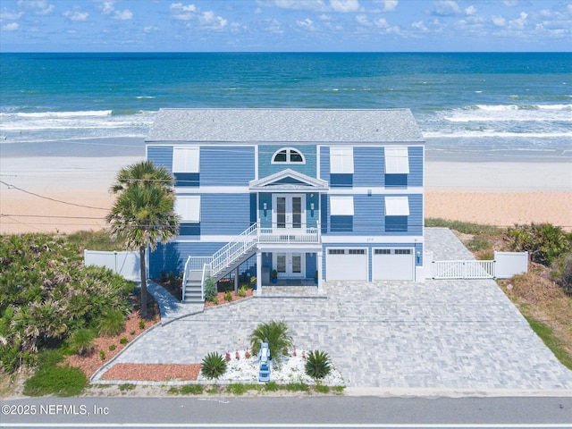 raised beach house with stairway, french doors, decorative driveway, an attached garage, and a gate