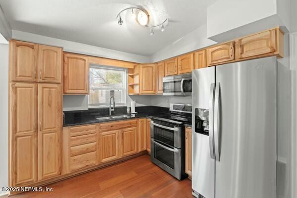 kitchen with dark countertops, a sink, appliances with stainless steel finishes, wood finished floors, and open shelves