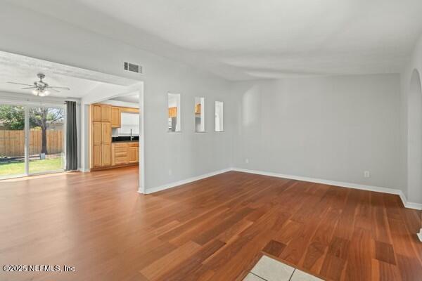 unfurnished living room featuring visible vents, ceiling fan, baseboards, wood finished floors, and a sink