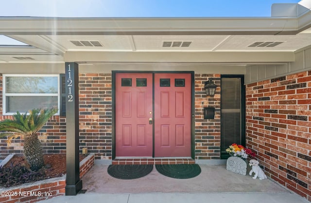 view of exterior entry featuring brick siding and visible vents