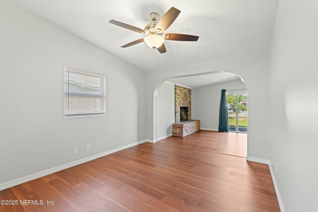 unfurnished living room with baseboards, arched walkways, lofted ceiling, and wood finished floors