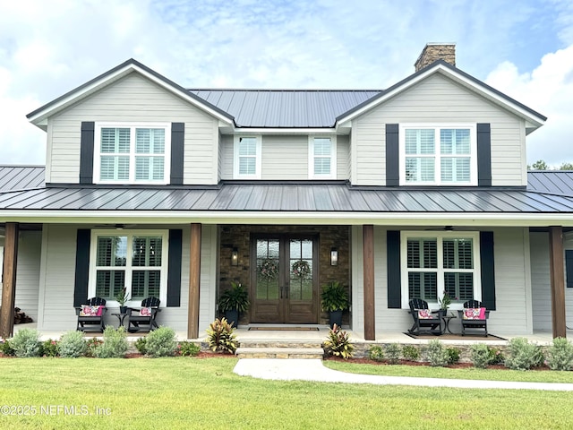 view of front of house with covered porch, french doors, metal roof, and a front yard