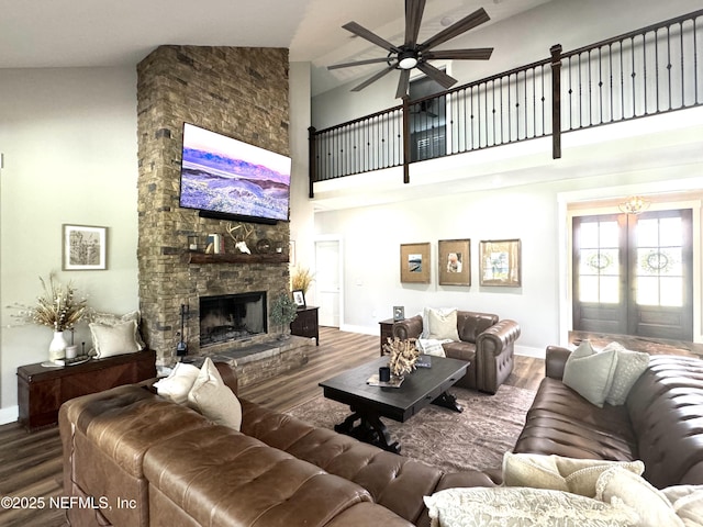 living room featuring baseboards, ceiling fan, a stone fireplace, a high ceiling, and wood finished floors