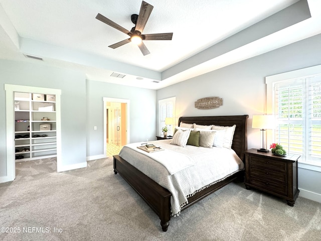 carpeted bedroom with visible vents, baseboards, a tray ceiling, ceiling fan, and a walk in closet