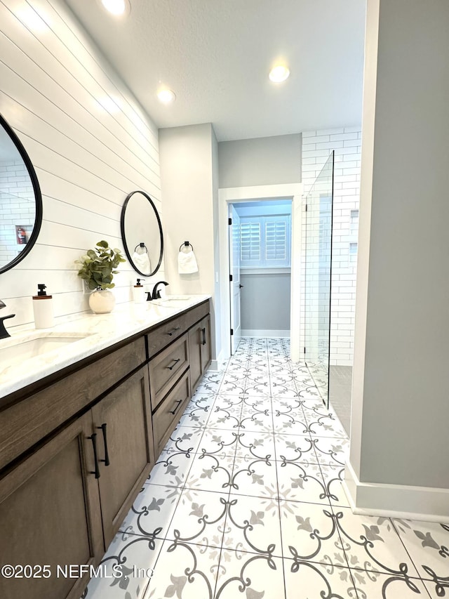 bathroom with a sink, baseboards, tiled shower, and double vanity