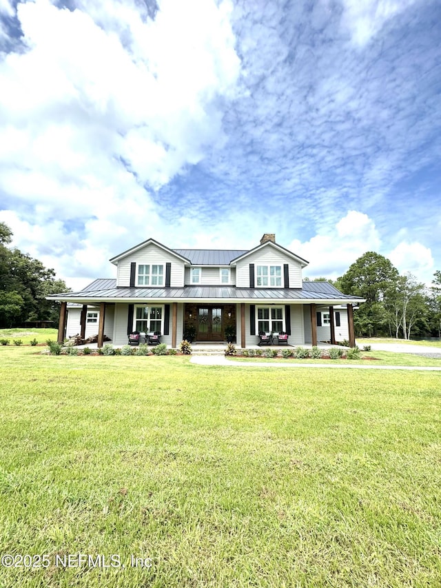 view of front of house with a standing seam roof, a porch, a chimney, a front lawn, and metal roof