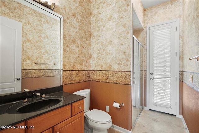 full bathroom with vanity, baseboards, wallpapered walls, a stall shower, and toilet
