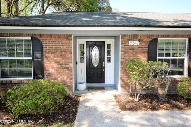 view of exterior entry featuring brick siding and roof with shingles