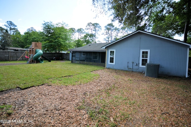 rear view of property featuring a sunroom, a lawn, fence, a playground, and central AC unit
