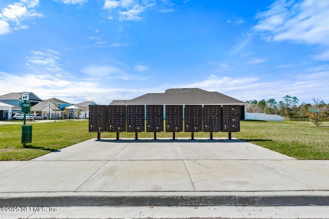 view of community featuring mail area, a lawn, and fence