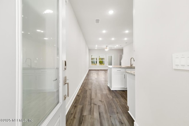 corridor featuring visible vents, baseboards, dark wood finished floors, recessed lighting, and a sink