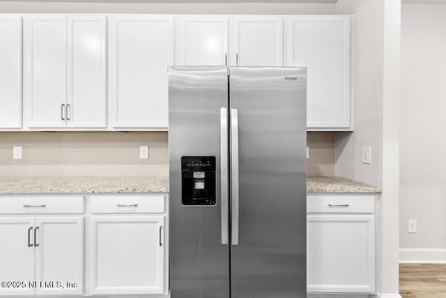 kitchen featuring light stone countertops, decorative backsplash, wood finished floors, stainless steel fridge, and white cabinetry