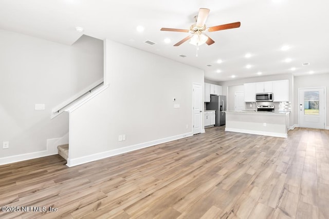 unfurnished living room with visible vents, light wood-style flooring, stairway, and a ceiling fan