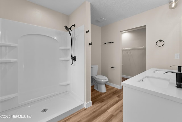 bathroom with wood finished floors, walk in shower, toilet, and a sink