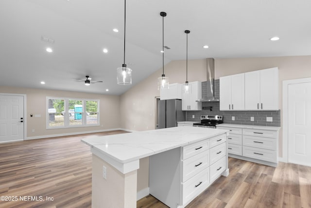 kitchen with stainless steel appliances, a center island, a ceiling fan, vaulted ceiling, and wall chimney range hood